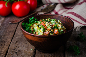 Fresh tabbouleh, a Middle Eastern salad, in clay bowl on wooden background. Selective focus. Toned...