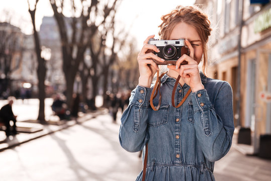 Concentrated woman taking pictures outdoors using old vintage camera