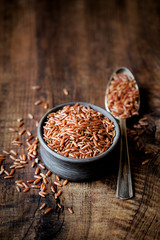 Red rice an a small ceramic bowl against dark rustic wooden background