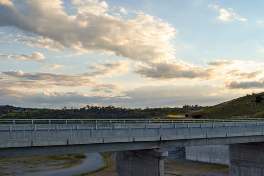 Kosciuszko Road running over the Jindabyne Dam wall with mountain view background and cloudscape.  Lake Jindabyne is part of the ground breaking 'Snowy Mountains Hydro-Electric Scheme'.