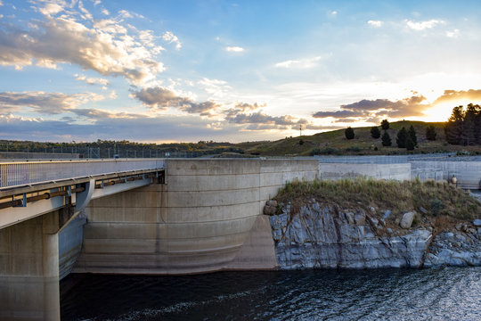 Kosciuszko Road running over the Jindabyne Dam wall with mountain view background and cloudscape.  Lake Jindabyne is part of the ground breaking 'Snowy Mountains Hydro-Electric Scheme'.