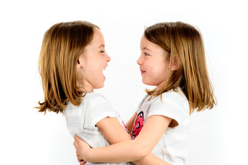 Twin girls are looking at eachother and smiling.