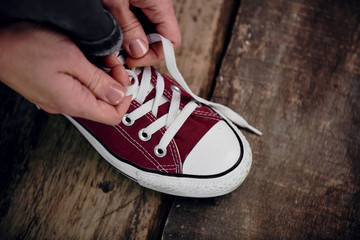 Close-up of teenage girl hands tying laces of red stylish gumshoes. Concept of travel, walk and adventure. 