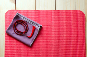 Accessories for yoga and meditation. Open mat and mala beads on wooden background with copyspace.