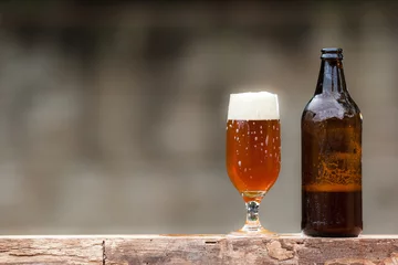 Rolgordijnen Bier Glass of beer and bottle on wood table