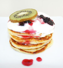 Pancakes with cream, berries and kiwi. Pancakes stacked on a white plate. Pancakes drizzled with whipped cream. A dessert of pancakes with cream, currants and kiwi. Pancakes with fresh berries.
