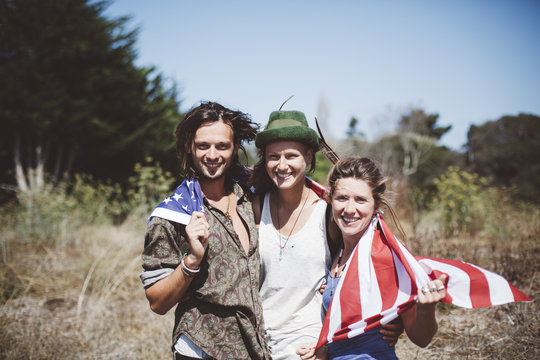 Portrait of three smiling hippies with US flag in the nature