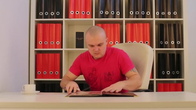 Man In Office Reading Catalog And Signing It