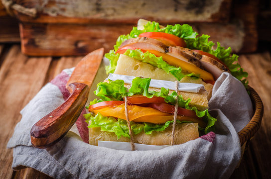 Homemade sandwich with fresh tomatoes and chicken breast in basket on wooden background. Selective focus. Picnic concept
