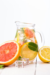 Homemade healthy water with grapefruit and ice in glass pitcher.