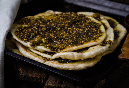Freshly baked flatbread with mixed spice and herbs - zaatar or zatar on vintage wooden background. Selective focus. Toned image