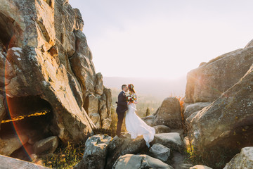 Portrait of romantic newlywed couple in yellow sunset lights on majestic mountain landscape with big rocks as backround © andrii kobryn