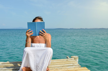 Girl reading a book sitting on a dock