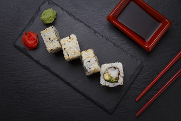 Sushi roll with ginger wasabi and soy sauce on a stone plate over black background