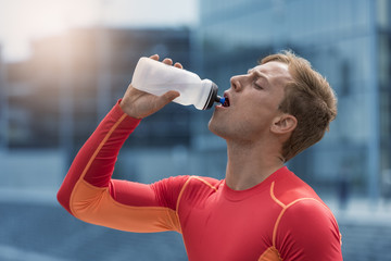 Athletic sportsman drinking energy drink. Running city man water