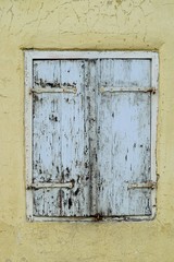 Altes Holzfenster mit geschlossenen Schlagläden in einem verfallenen, sanierungsbedürftigen Haus