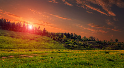 Fototapeta na wymiar Rural landscape with a hill. Green meadow under sunset, colorful sky with clouds Dramatic morning scene. Beautiful natural landscape