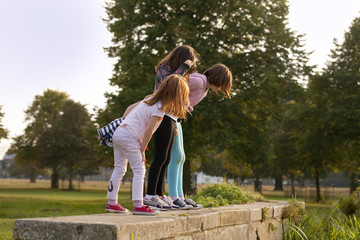 Obraz premium Three Tomboys. Three sisters are peering over a wall in a local park interested to see what is on the other side. The two older girls stand quite confidently while the younger is more hesitant.