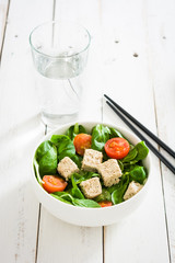 Vegan tofu salad with tomatoes and lamb's lettuce in bowl on white wood
