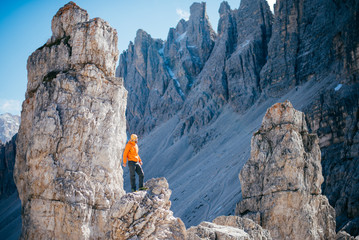 The young brave climber in orange jacket rises to the top of the rocky mountains in the Alps