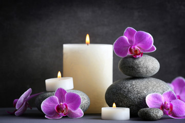 Composition of spa pebbles, flowers and candles on grey background