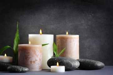 Composition of spa pebbles, candles and bamboo leaf on grey background