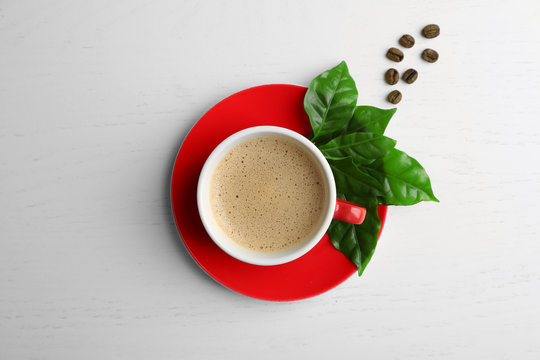 Cup of coffee with beans and leaves on light background