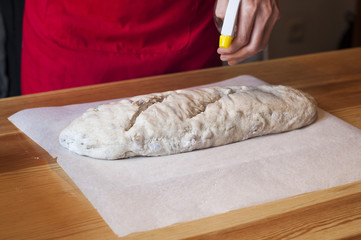 Homemade bread: female hands kneading dough. Spraying water before put in the oven.