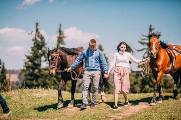 Young couple walking with two horses in the mountains