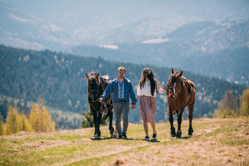 Young couple walking with two horses in the mountains