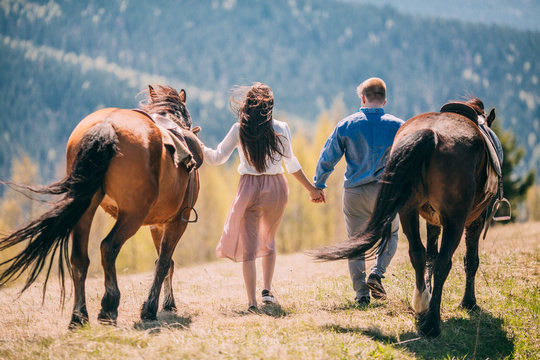 Young Couple Walking With Two Horses In The Mountains