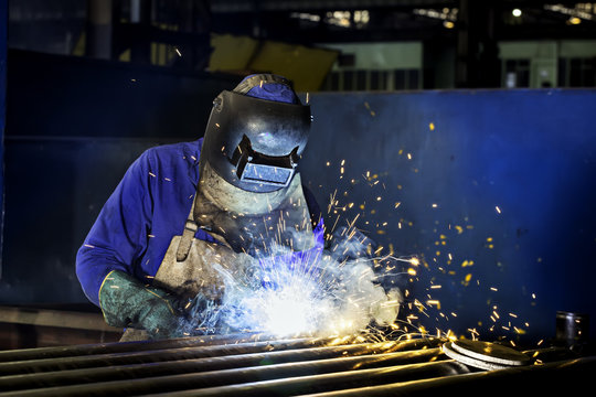 Worker dressed in protective uniform welding metal frame