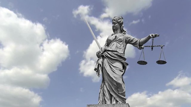 Statue of Lady Justice in front of moving clouds