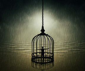 Man standing closed in a bird cage with wide opened hands in front of the ocean horizon in a rainy day. Life limitation, trapped in a prison concept 