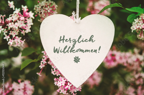 "Herzlich Willkommen! Weißes Herz mit Schrift und Blumen" Stockfotos