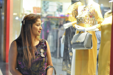 Fototapeta na wymiar Woman eyeing Indian suits in clothing shop. A beautiful young Indian woman looking at the display showcase of a clothing shop at the mall for shopping.