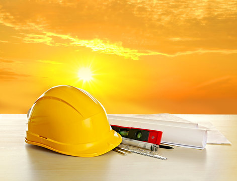 Table with construction drawings and other tools on sunrise background