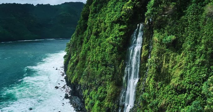 Aerial view revealing amazing waterfall hidden in a tropical rain forest along the coastline sea cliffs