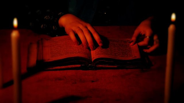 A female witch considers an old book on a table with burning candles. Shooting with the shallow depth of field