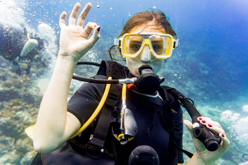 Frau beim Tauchen im Urlaub an Korallen Riff gibt das OK Zeichen - obrazy, fototapety, plakaty