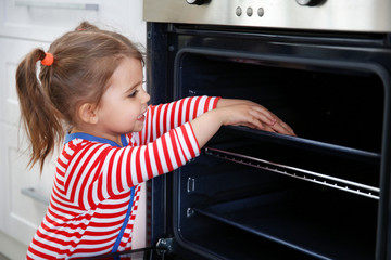 Fototapeta na wymiar Little girl playing with oven in the kitchen