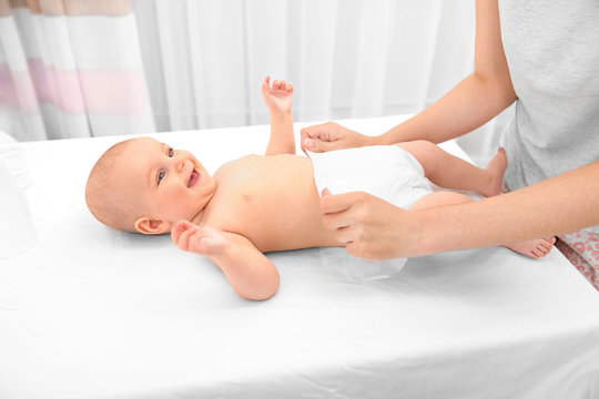 Mother changing diaper to little baby in room