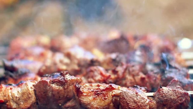 Grilling barbecue meat on wood coal. Man turns skewers. Man cooks appetizing hot shish kebab on metal skewers. Tasty meat pieces with crust. Grilling food. Cooking shashlik on barbecue grill. Closeup