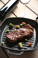 Grilled steak on grill pan with wine on wooden table