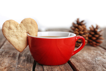 Heart shape cookie on cup of coffee on wooden table closeup