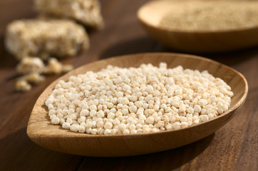 Popped white quinoa (lat. Chenopodium quinoa) cereal on small wooden plate, photographed on wood with natural light (Selective Focus, Focus one third into the quinoa cereal)