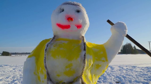 A colorful snowman with yellow shirt on it. The snowman has a long nose and red mouth