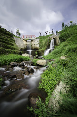 Fototapeta na wymiar beautiful scenery of hidden waterfall with cloudy sky in the middle of tea farm at Cameron Highland, Malaysia.Soft focus and some motion blur due to long exposure. Focus in the center