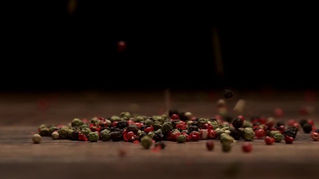 Mixed peppers falling on a wooden table on a black background. Slow motion. Close up