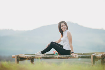 Fototapeta premium Smiling teenage girl sitting on bamboo bench.